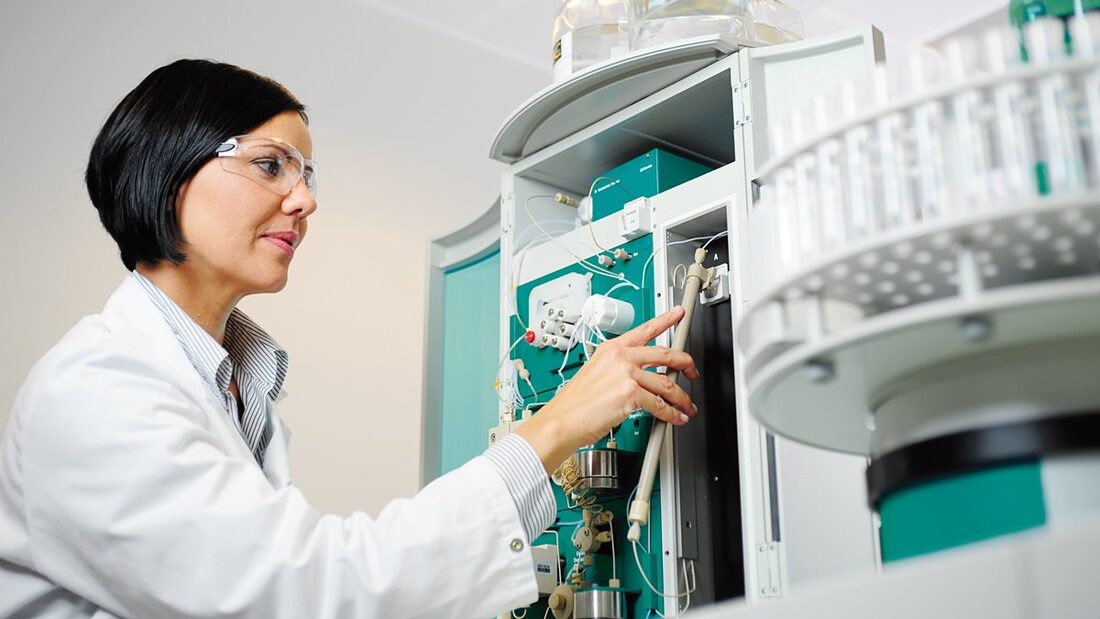 woman in laboratory with ion chromatograph in the background and an IC column in the hand